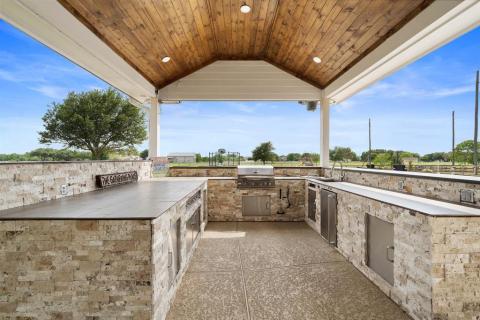 The nicely Lit Covered Outdoor kitchen with a Sink, drawers, Refrigerator, Grill, and lots of cabinet & counter space.