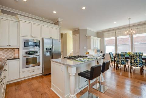 The wall of windows, right, provides great natural light for a spacious breakfast/casual dining nook. Note the 5- burner gas stove, and look for the appealing farmhouse style sink and huge walk-in surrounding pantry.