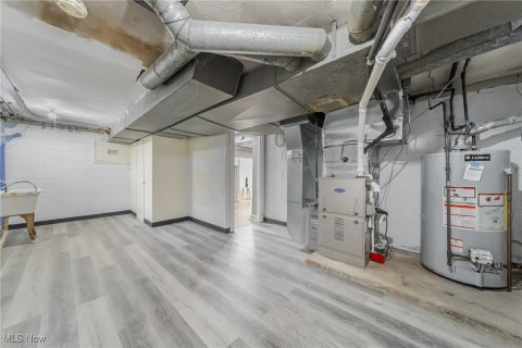 Basement with sink and light LVT Flooring, gas water heater, and heating unit