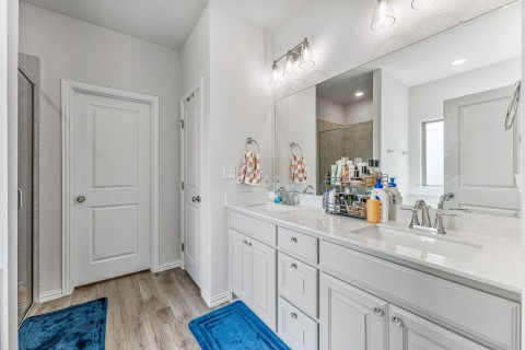 Bathroom with hardwood / wood-style flooring, double sink vanity, and a shower with shower door