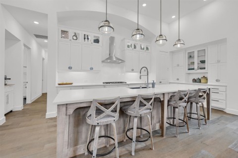 Kitchen with pendant lighting, sink, white cabinetry, a spacious island, and wall chimney exhaust hood