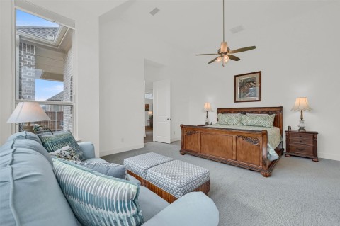 Bedroom featuring ceiling fan, light colored carpet, and a high ceiling