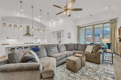 Living room with ceiling fan, sink, light hardwood / wood-style flooring, and a high ceiling