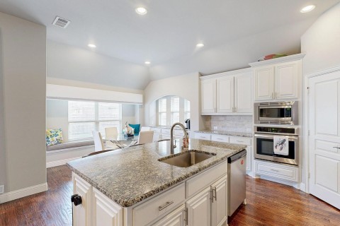 Kitchen featuring wood-style flooring, a sink, visible vents, vaulted ceiling, and appliances with stainless steel finishes and lots of counter top space.