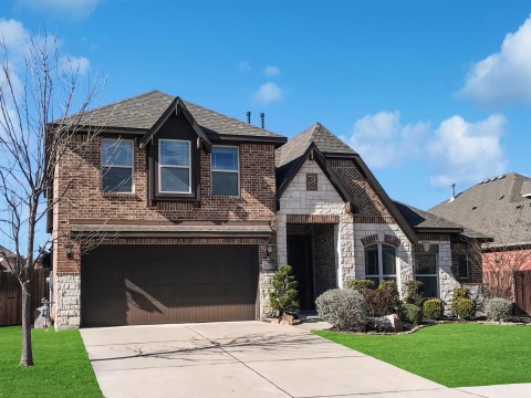 View of front facade with stone siding, brick siding, fence, and established front lawn