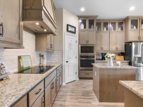 Kitchen featuring stainless steel appliances, backsplash, light wood-style floors, granite countertops, and custom range hood
