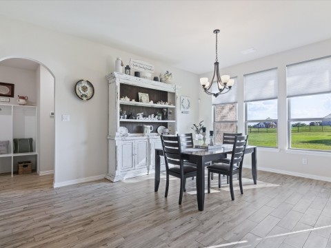 Dining room featuring light wood-style flooring, baseboards, arched walkways, and a chandelier with natural lighting