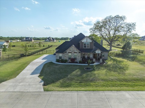 View of front facade featuring stone siding, a front lawn, concrete driveway, and fence