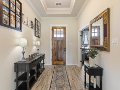 Entrance foyer featuring a raised ceiling, crown molding, baseboards, and light wood-style flooring with study access