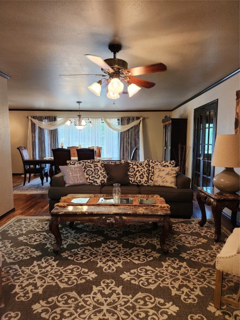 Living room featuring wood-type flooring, a textured ceiling, and ceiling fan with notable chandelier