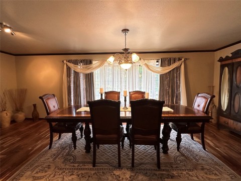Dining area featuring crown molding, a textured ceiling, wood-type flooring, and a notable chandelier