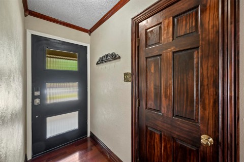 Doorway to outside featuring a textured ceiling, ornamental molding, and dark hardwood / wood-style flooring