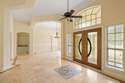 Spacious, elegant entryway with high ceilings and abundant natural light. Features decorative tile flooring, a stylish ceiling fan, and distinctive glass double doors flanked by large windows. Ideal for a welcoming home atmosphere.