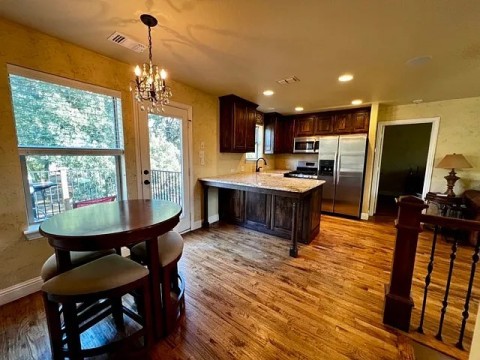 Kitchen featuring stainless steel appliances, wood finished floors, a peninsula, a chandelier, and recessed lighting