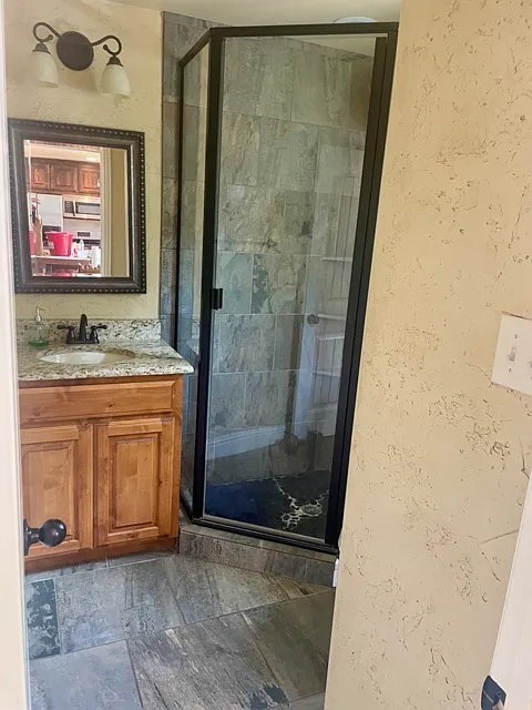 Full bathroom with a textured wall, vanity, and a shower stall