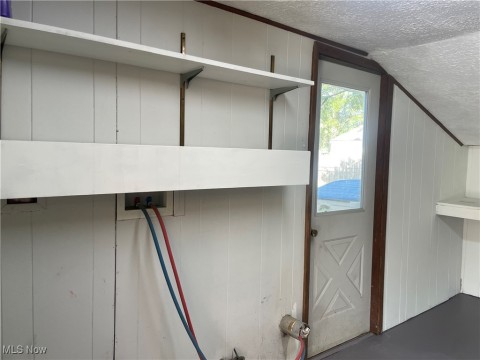 Laundry room view of a textured ceiling, concrete floors, and a decorative wall