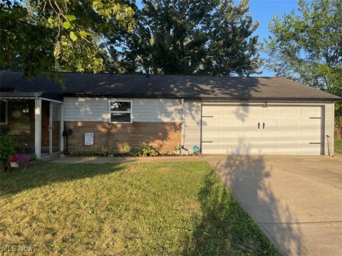 View of front of property featuring a garage, a front lawn, roof with shingles, and driveway