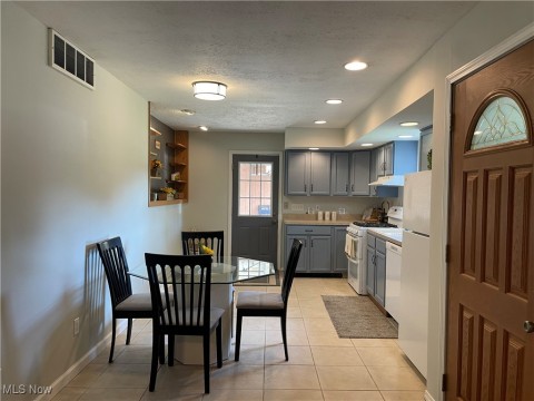 Kitchen with gray cabinetry, white appliances, light tile patterned flooring, light countertops, and a textured ceiling