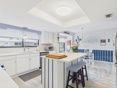 Kitchen with white cabinets, decorative light fixtures, a kitchen island, a tray ceiling, and a breakfast bar