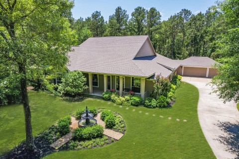 Charming single-story home with a welcoming front porch, nestled in a lush, landscaped yard. Features includes well-maintained landscaping, a decorative fountain, and a serene, wooded backdrop. Perfect for those seeking tranquility and curb appeal.