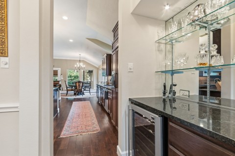 This photo showcases a stylish bar area with glass shelving, a granite countertop and a beverage refrigerator. Located adjacent to a laundry room with plenty of cabinets for your storage.