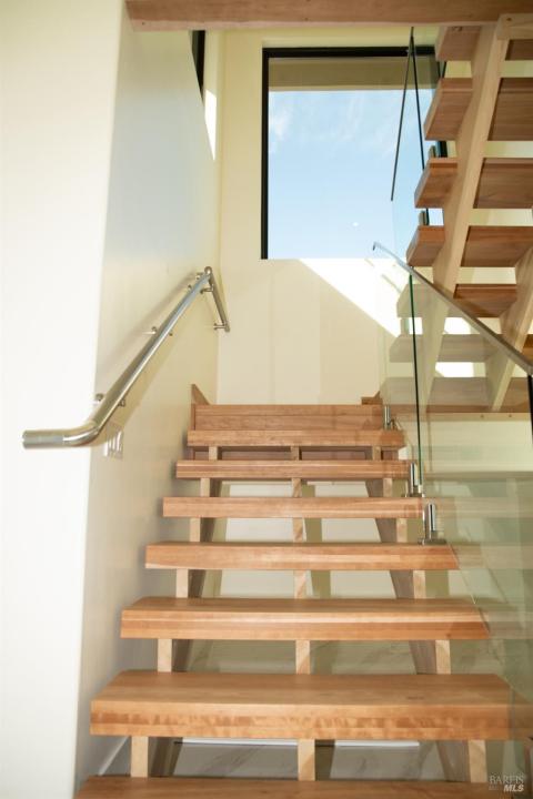 Steps going upstairs guarded by clear glass panels and stainless steel handrails.
