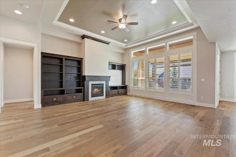 Unfurnished living room featuring a raised ceiling, a ceiling fan, a lit fireplace, recessed lighting, and light wood finished floors