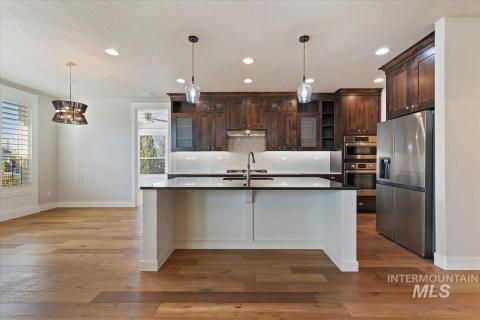 Kitchen with stainless steel appliances, tasteful backsplash, hanging light fixtures, dark brown cabinetry, and a kitchen bar
