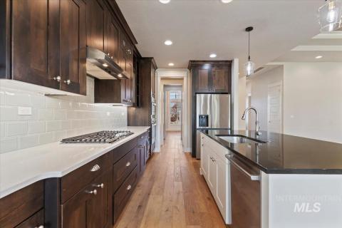 Kitchen featuring dark brown cabinets, light wood-style floors, dark stone countertops, decorative light fixtures, and under cabinet range hood