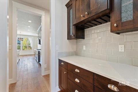 Bar area featuring dark brown cabinets, backsplash, light wood-type flooring, light stone counters, and a textured ceiling