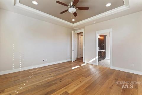 Master bedroom with a raised ceiling, light wood-style flooring, recessed lighting, ceiling fan, and connected bathroom