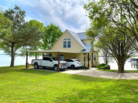 Charming two-story lakeside home with a covered carport and mature trees, offering serene water views and a private dock.