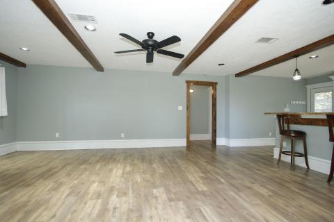 This spacious living area features laminate wood flooring, exposed ceiling beams, and a ceiling fan. This spacious living area features laminate wood flooring, exposed ceiling beams, and a ceiling fan.