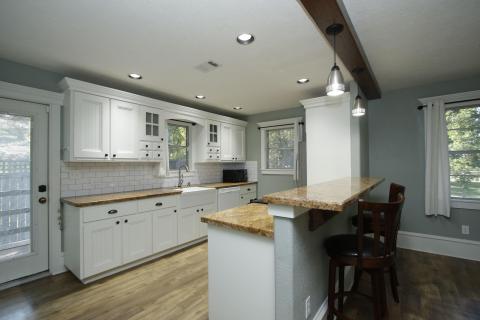 This modern kitchen boasts an open layout with sleek white cabinetry, gorgeous countertops, and a subway tile backsplash. Enjoy the convenience of a breakfast bar with stylish pendant lighting, abundant natural light, and warm laminate wood flooring. This modern kitchen boasts an open layout with sleek white cabinetry, gorgeous countertops, and a subway tile backsplash. Enjoy the convenience of a breakfast bar with stylish pendant lighting, abundant natural light, and warm laminate wood flooring.