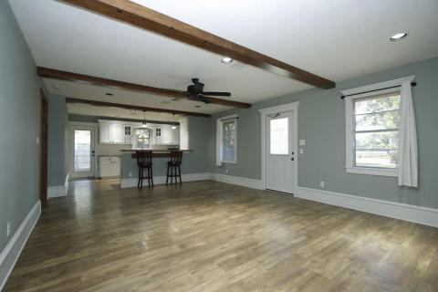 Spacious, open-plan living area with laminate wood flooring, exposed ceiling beams, and a ceiling fan. The room connects to a kitchen with a breakfast bar providing a cozy and inviting atmosphere. Natural light fills the space, highlighting the modern and clean design. Spacious, open-plan living area with laminate wood flooring, exposed ceiling beams, and a ceiling fan. The room connects to a kitchen with a breakfast bar providing a cozy and inviting atmosphere. Natural light fills the space, highlighting the modern and clean design.