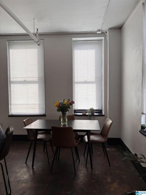 Interior space featuring exposed ceiling piping, high ceilings, large windows with blinds, a dark floor finish, and white walls with dark trim