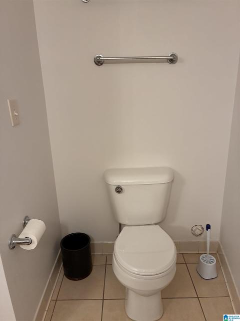 White toilet in a neutral-toned room featuring a chrome towel bar, coordinating toilet paper holder, and light tile flooring