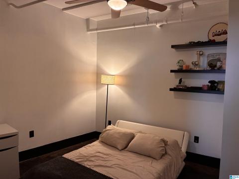 White walls with a contrasting dark baseboard, dark wood-finish flooring, and a ceiling fan with integrated lighting