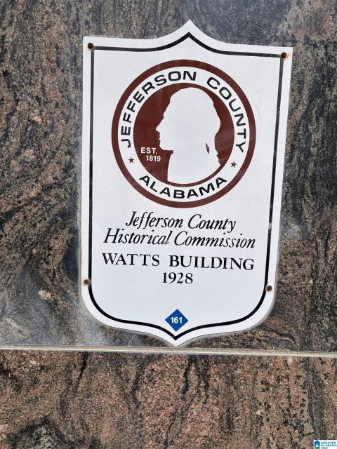 Historical marker for the Watts Building, established in 1928, set against a polished granite-look surface