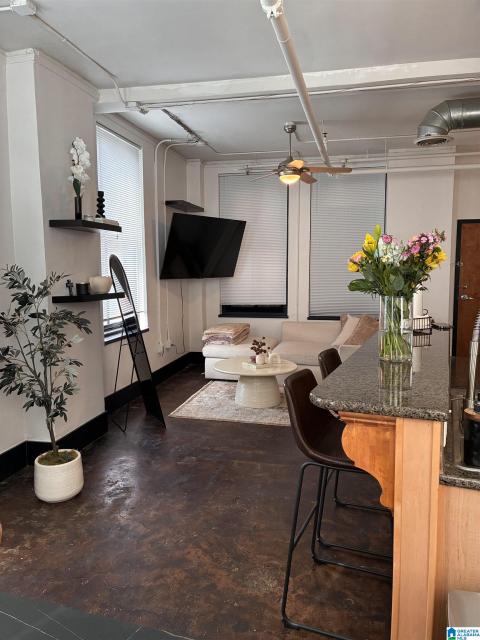 Open-concept living area with dark concrete flooring, exposed ceiling conduit, and a ceiling fan