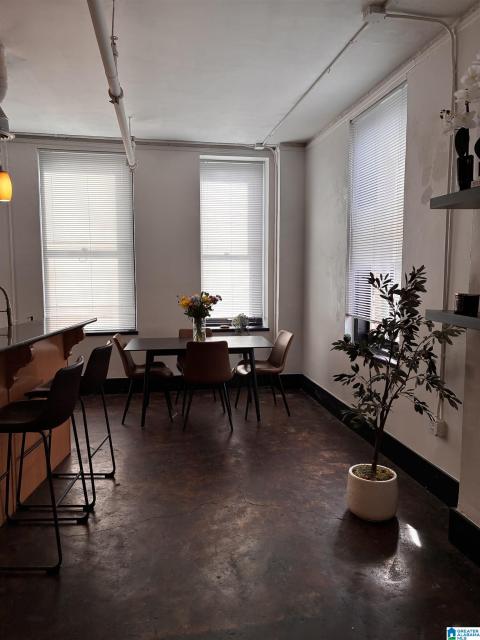 Open-concept space featuring industrial-style exposed conduit, high ceilings, and multiple windows with blinds