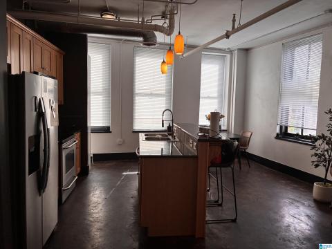 Kitchen featuring exposed ceiling pipes, stainless steel appliances, wood-finish cabinetry, a central island with integrated sink, and abundant natural light from multiple windows