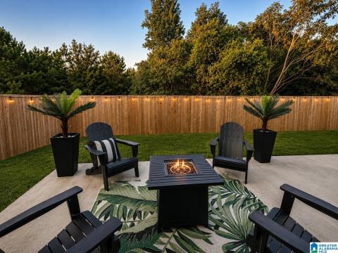 Spacious concrete patio with a fire pit feature, surrounded by a wood privacy fence, string lighting, and a manicured lawn