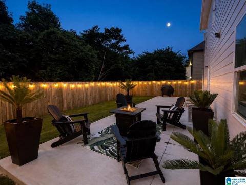 Expansive concrete patio with a fire pit, bordered by a wooden privacy fence, string lighting, and landscaping