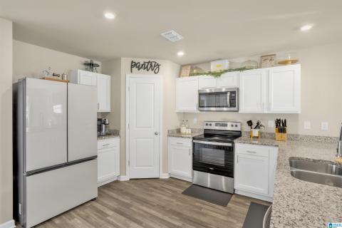 Modern kitchen featuring white cabinetry, granite-finish countertops, stainless steel appliances, and wood-finish flooring