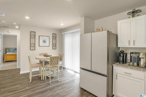 Open-concept kitchen and dining area featuring wood-finish flooring, white cabinetry, a stainless steel refrigerator, and a sliding glass door