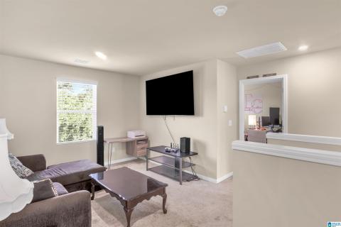 Modern living room featuring wall-mounted flat-screen television, neutral carpet flooring, and recessed ceiling lighting